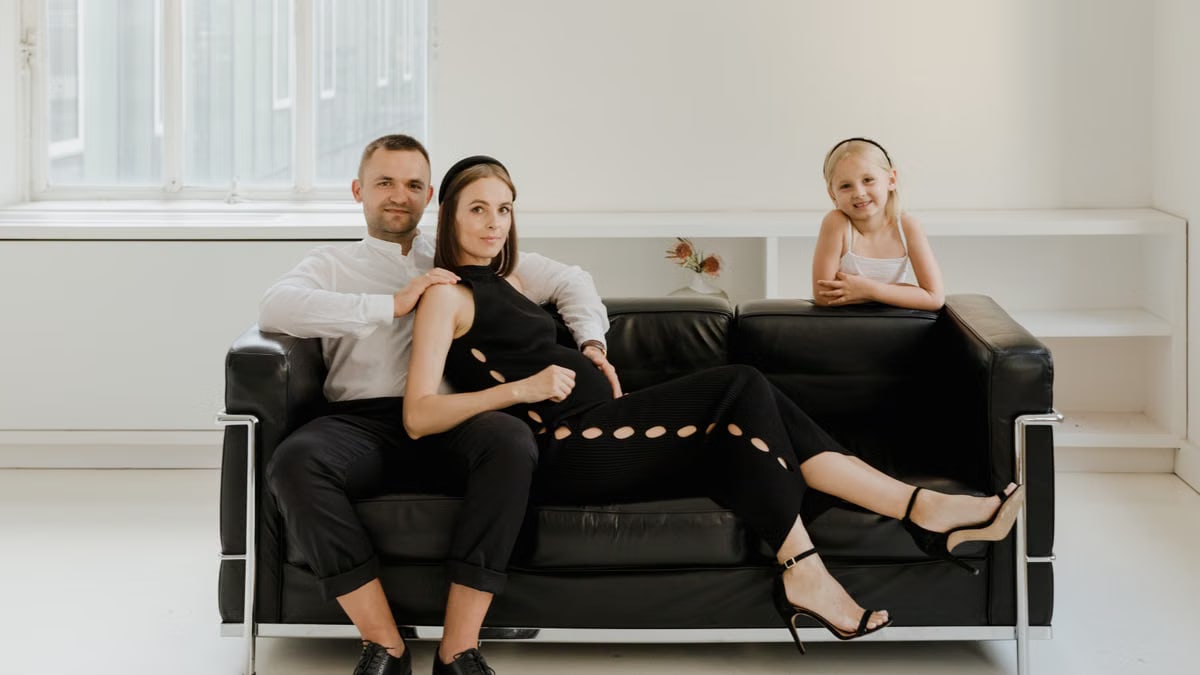 Elegant family photo on a modern sofa, featuring a couple and child dressed in black and white.